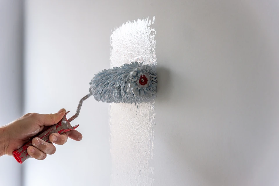 Une personne applique de la peinture blanche sur un mur gris à l'aide d'un rouleau à peinture