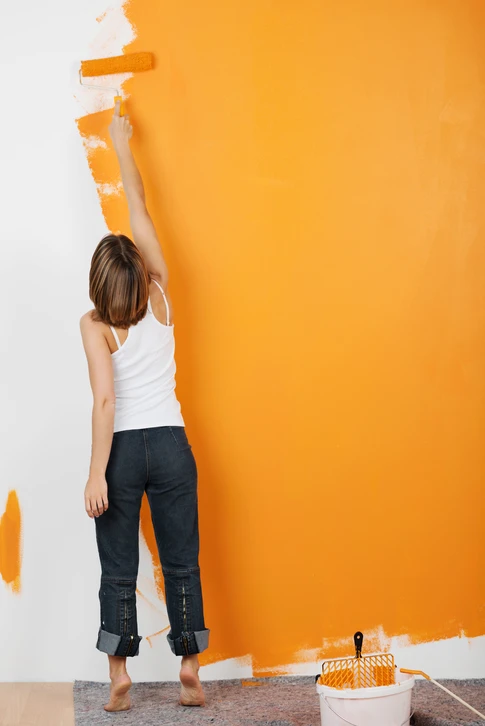 Femme peignant un mur intérieur avec un rouleau, appliquant de la peinture orange vif sur surface blanche