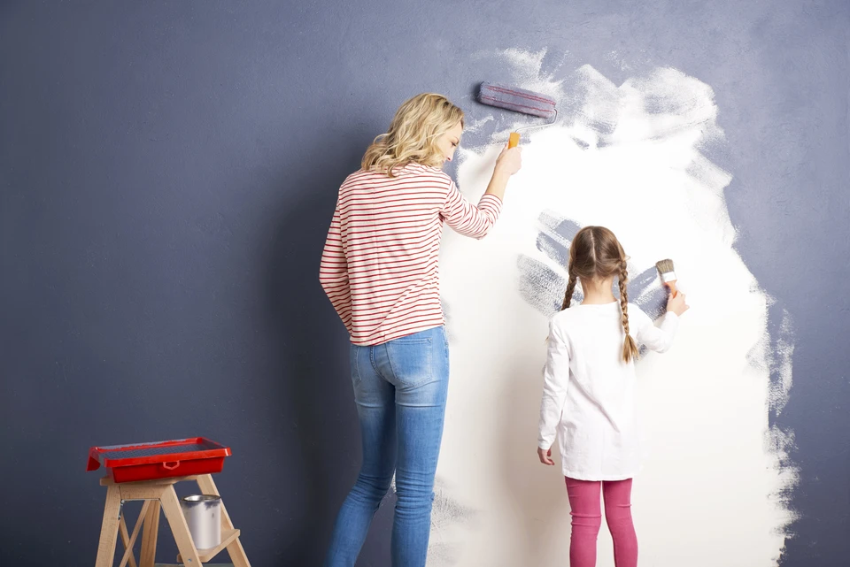 Mère et fille peignent ensemble un mur intérieur, appliquant de la peinture blanche sur une surface bleu-gris