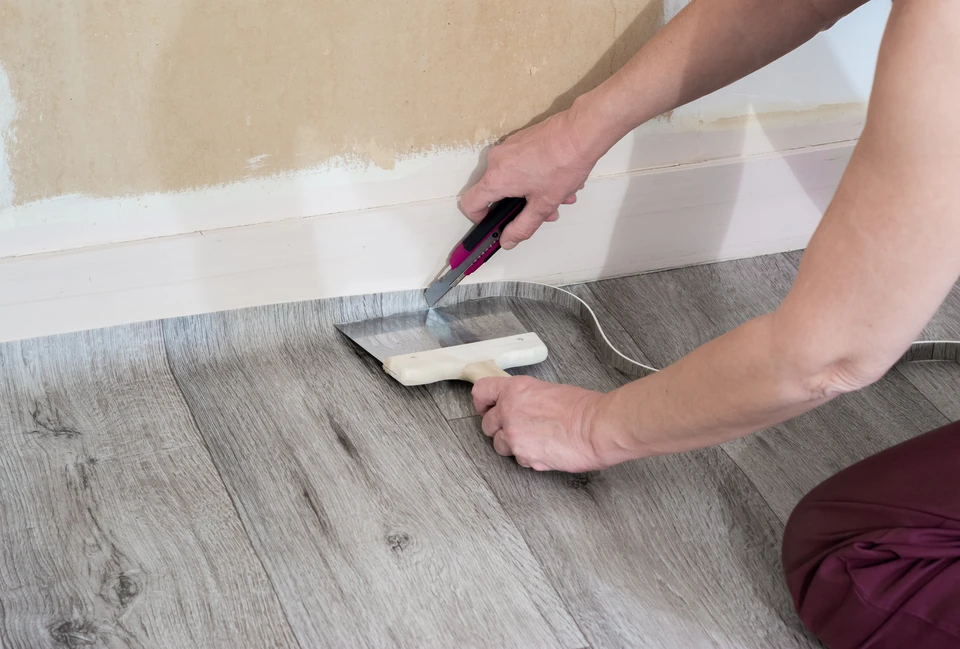 Un homme agenouillé mesure un parquet en bois foncé avec un mètre ruban jaune